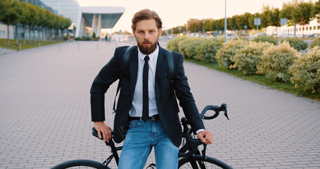 Close up of handsome serious modern stylish man with beard which sitting on his bike on pedestrian...