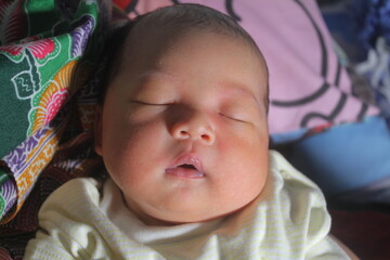 Portrait of a two month old boy looking at camera cutely and smiling as he sleeps in brown clothes in newborn baby photo shoot
