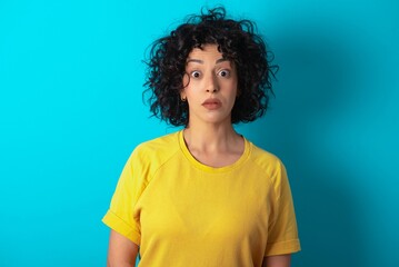 Stunned Young arab woman wearing yello T-shirt over blue background stares reacts on shocking news....