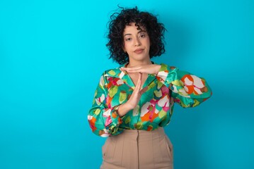 young arab woman wearing colorful shirt over blue background being upset showing a timeout gesture, needs stop, asks time for rest after hard work,