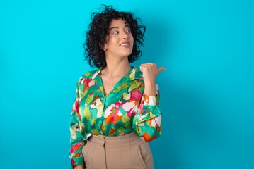 Charming young arab woman wearing colorful shirt over blue background looking at copy space having advertisements