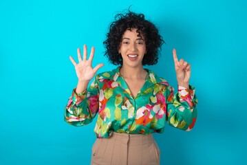 young arab woman wearing colorful shirt over blue background showing and pointing up with fingers...