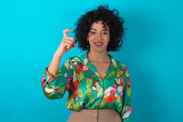 young arab woman wearing colorful shirt over blue background pointing up with fingers number nine in Chinese sign language Jiu