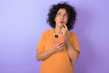 young arab woman wearing yellow T-shirt over purple background thinks deeply about something, uses...