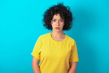 Fototapeta na wymiar young arab woman wearing yellow T-shirt over blue background Pointing down with fingers showing advertisement, surprised face and open mouth