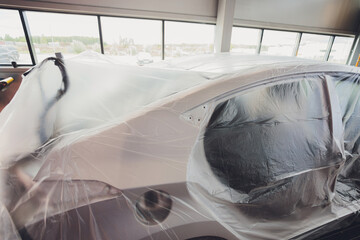 A broken car color silver, wrapped in a plastic coating. The car is covered with polyethylene after...