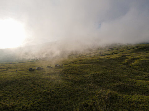 Drone view four offroad cars on the Tambora mountain savanna on a foggy afternoon before sunset