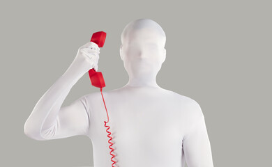 Person in faceless bodysuit disguise makes anonymous incognito phone call from unknown number. Strange unrecognizable young man wearing white spandex costume holding red vintage telephone receiver - obrazy, fototapety, plakaty