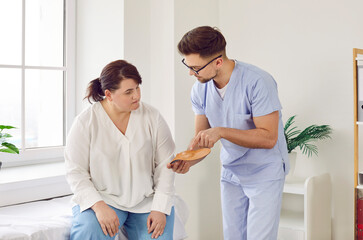 Fototapeta premium Man doctor podiatrist at the clinic gives comfortable orthotic medical insoles for orthopedic shoes to a young overweight woman patient. Feet health, flat foot prevention concept