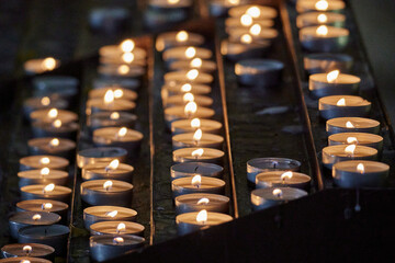 Close-up shot of multiple lit votive candles in a church setting, with a blurred out background