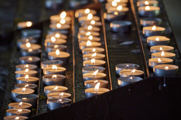 Close-up shot of multiple lit votive candles in a church setting, with a blurred out background