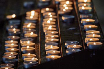 Close-up shot of multiple lit votive candles in a church setting, with a blurred out background