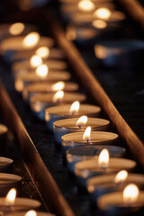 Close-up shot of multiple lit votive candles in a church setting, with a blurred out background - obrazy, fototapety, plakaty