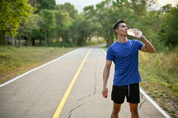 Thirsty and exhausted Asian man in sportswear drinks water from a bottle while running