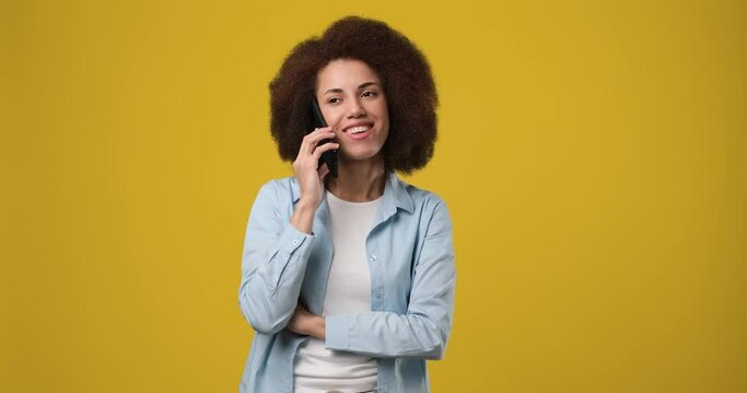 Young beautiful smiling African american woman talking on the phone answering phone call over yellow orange background