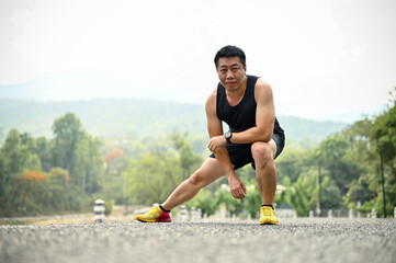 Sporty mature Asian man in sportswear stretching his legs, side lunges