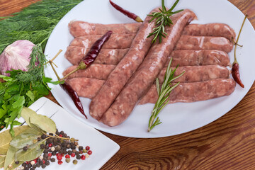 Raw sausages among spices and greens on dish close-up