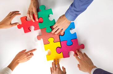Group of three young people place colorful puzzles on table and present the concept of cooperation, teamwork, support and assistance in the office. Hands close-up of office workers assembling puzzle.
