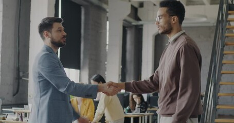 Men partners talking and shaking hands standing in shared office enjoying successful cooperation. Businesspeople and cooperation concept.