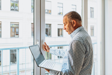 Attractive man in shirt standing near window with laptop