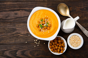 Autumn Vegetarian pumpkin and carrot cream soup with chickpeas and herbs on dark wooden background. Comfort food, fall and winter healthy slow food concept.