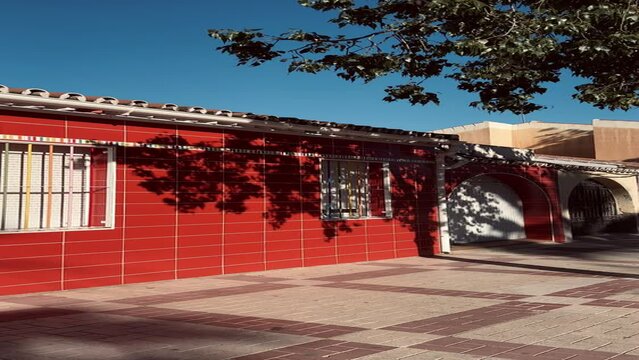 Red building in Spain with tree leaves' shadows on it. Vertical video 