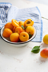 Fresh ripe apricots in bowl close up on light surface