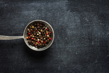 Big old spoon with peppercorn on black background
