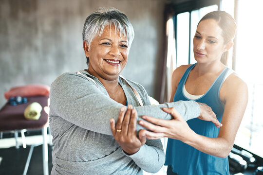 Stretching, support and old woman with personal trainer for fitness, wellness or rehabilitation. Health, workout or retirement with senior patient and female trainer in gym for arm warm up training - Powered by Adobe
