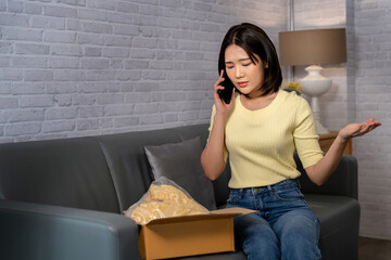 Young Asian woman complaining on mobile phone when she received a wrong or damaged parcel from...