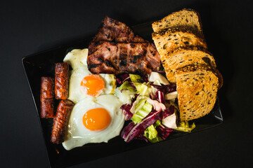 Top view - English breakfast with eggs sausages and bacon on black background