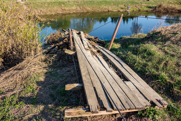 Fototapeta na wymiar Broken wooden suspension bridge spanning a river in the countryside