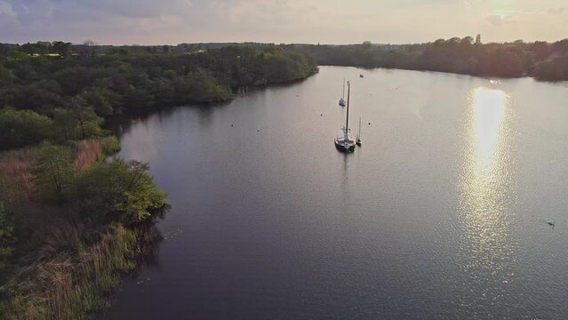  High up aerial shot of two traditional sailing boats moored on Wroxham Broad, a body of water in the heart of the Norfolk Broads National Park. Captured on a bright evening as the sun starts to set