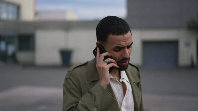 One concerned young Middle Eastern man speaking on phone outside in city street. A serious Arab male person talking on smartphone conversing