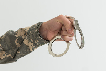 A military man in handcuffs holds an army badge in his hand on a dark background, selective focus....