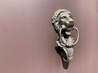 Vintage bronze knocker door handle in the shape of a lion's head with ring in his mouth on the old weathered brown painted metal gate. Close up.