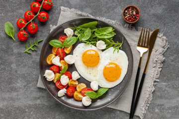 Fried eggs and Caprese salad with tomatoes, mozzarella cheese and basil leaves in a plate. Top view.