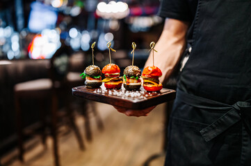 Waiter hold set mini hamburgers, mini burgers on plate in restaurant - obrazy, fototapety, plakaty