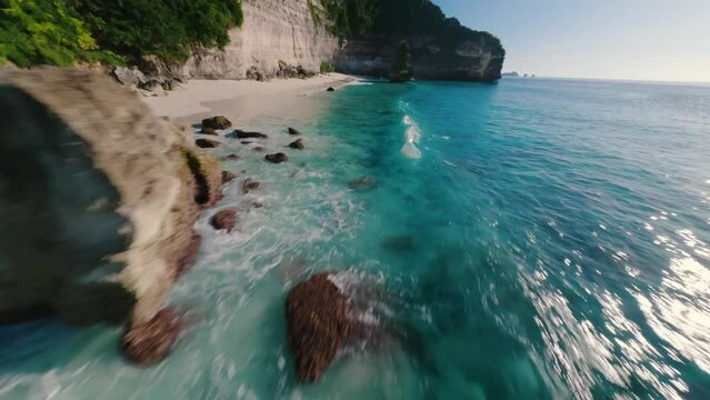 Spectaculair FPV drone aerial of a cliff spinning into tropical bright waters, circling a rock on sunny beach dream destination. Ultimate summer vibes, horizontal shot in Suwehan