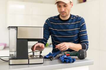 Professional young repairman repairs a coffee maker. Handsome worker in uniform repairing coffee machine in a workshop.