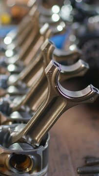 Vertical video. Engine pistons with connecting rods stand in a row. The camera focuses on them. Spare parts in a car service.