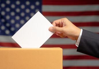 Hand voter holding ballot paper putting into the voting box at place election against the American flag background