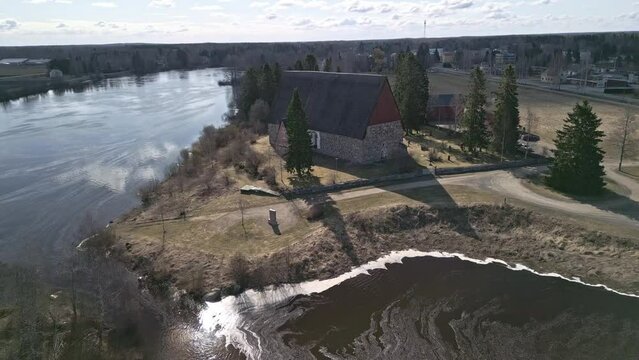 Old finnish stone churh going in with drone for far. Beside river. In spring.