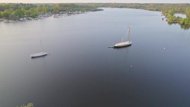 Aerial orbit shot over Wroxham Broad, a body of water in the heart of the Norfolk Broads National Park. Captured on a bright summer evening as the sun starts to set
