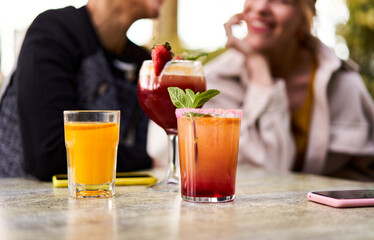 Three glasses of Natural cocktails or Mocktails on a table surrounded by a group of unrecognisable female friends gathering outside a bar in a terrace. Copy space image.