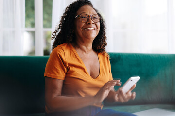 Retires senior woman using a smartphone to stay connected at home - obrazy, fototapety, plakaty