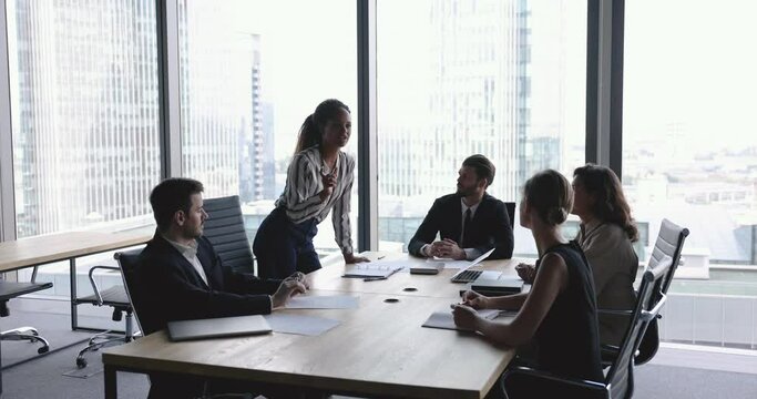 Five multiracial business people take part in group meeting, briefing led by young and ambitious African female boss. Formal negotiations, company management brainstorming in modern conference room