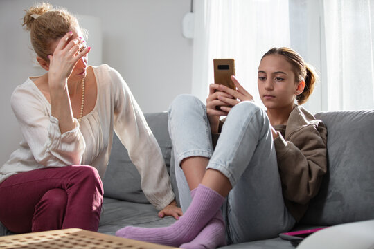 Mother having trouble with a lazy teenager girl at home while playing video games on a smartphone.