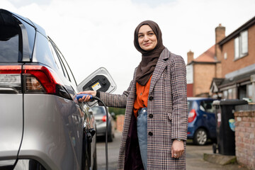 Woman wearing hijab charging electric car © Cultura Creative