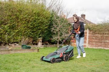 Woman wearing hijab mowing grass in backyard